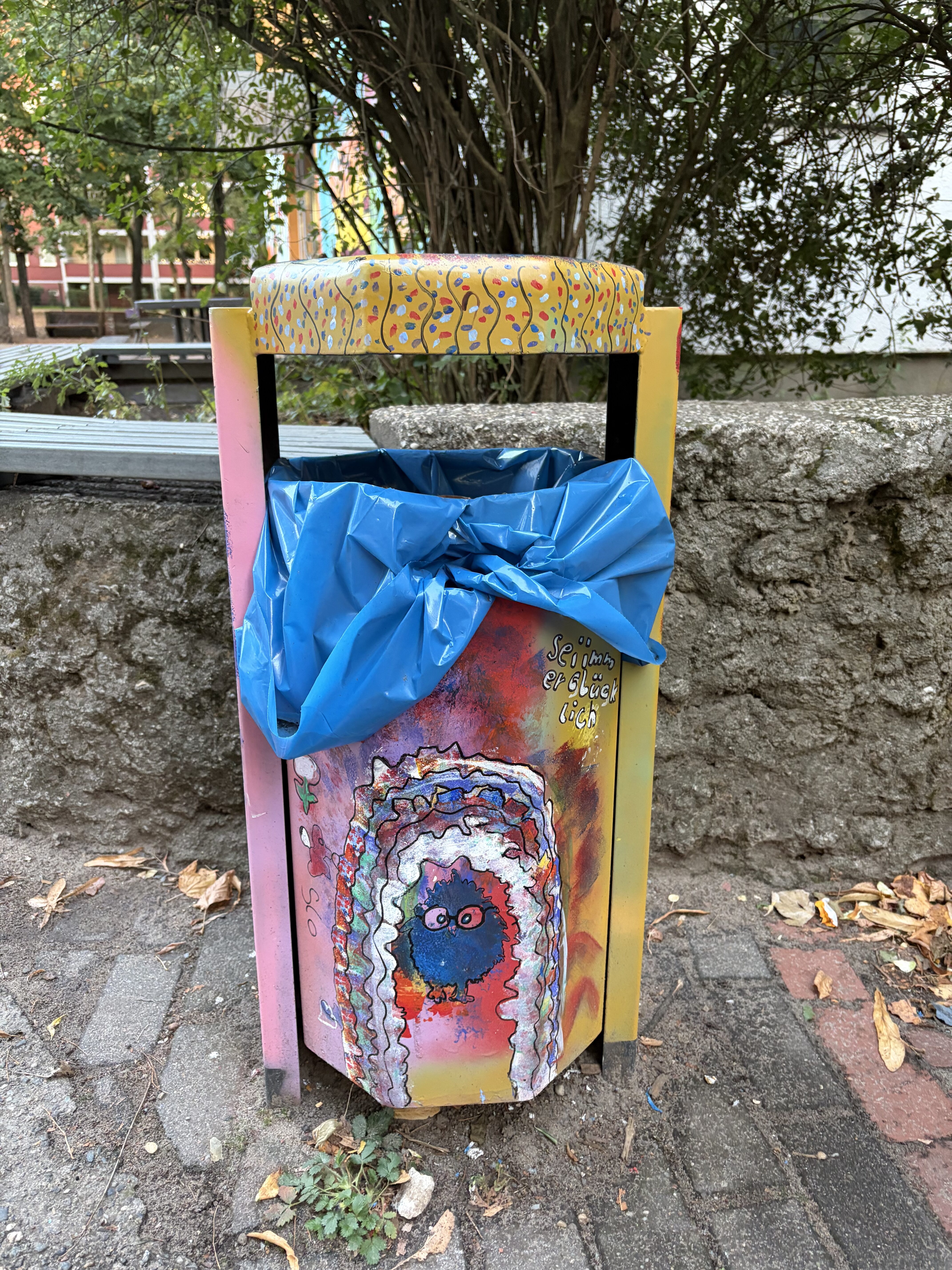 Bunt gestalteter Mülleimer mit gelbem Rand und fantasievoller Figur